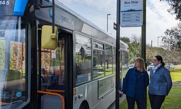 Cllr Joy Dennis, Cabinet Member for Highways and Transport (left), with county council officer Liz Robbins, who is leading on the rollout of the new Real Time Passenger Information displays. They are pictured at a bus stop in Barnham Road, Eastergate. Cllr Dennis is testing the audio push-button facility, which will make bus travel easier for passengers with visual impairments, learning or reading difficulties.