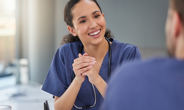 Female in nurses uniform engaged in a work meeting, talking enthusiastically to team member.  