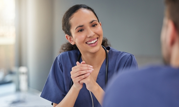 Female in nurses uniform engaged in a work meeting, talking enthusiastically to team member.