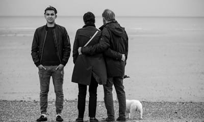 Young boy standing on beach with foster carers, looking out to sea