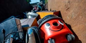 A vacuum cleaner, kettle and other waste electrical items in a container at a recycling centre.