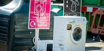 Washing machine placed by a large appliances sign at a recycling centre.