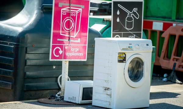 Washing machine placed by a large appliances sign at a recycling centre.