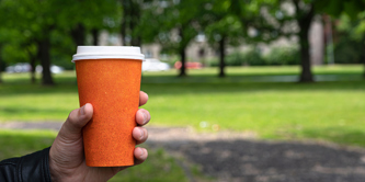 Person holding takeaway coffee cup in a park.
