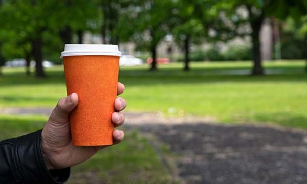 Person holding takeaway coffee cup in a park.