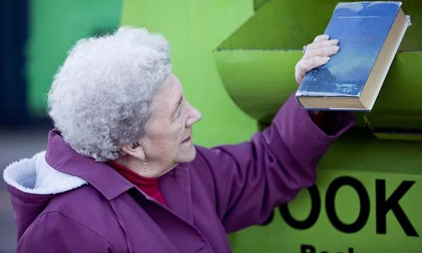 Lady placing a book in a book recycling container.