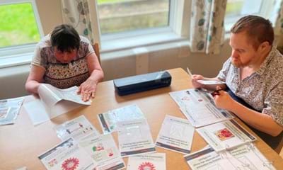 Two people sat at a table working on a COVID19 booklet produced by residents at Hobbs Field residential home