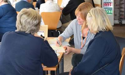 Two ladies sit at a table and answer questions while a council officer writes down their responses.