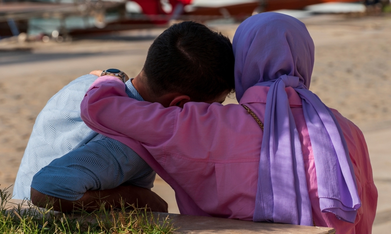 Two people sitting down with one person hugging the other