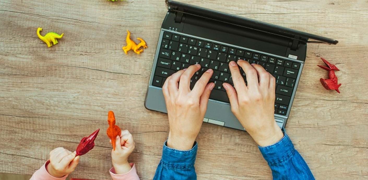 nojs A person's hands on a laptop keyboard with a child's hands playing with toys