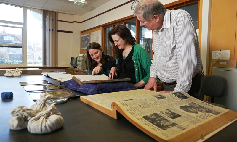 Several people looking at a number of documents spread out over a large table. 