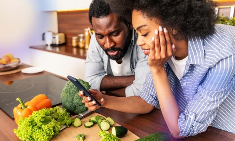 Man and woman look at phone while preparing food.