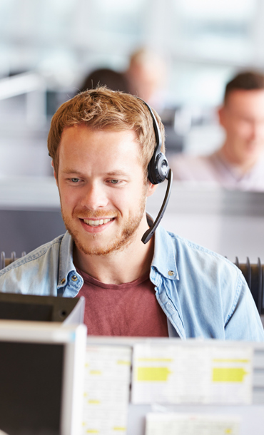 A man wearing a telephony headset sat at a desk in a call centre.