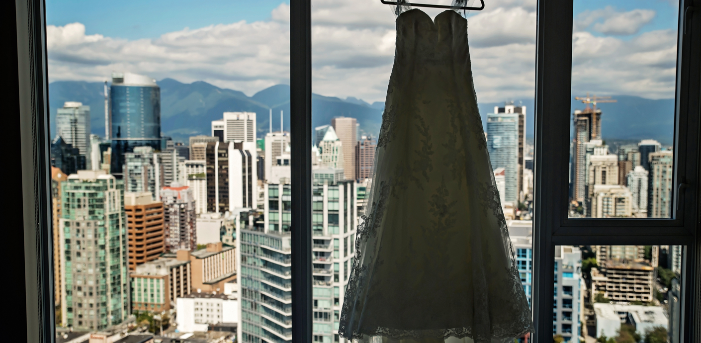 nojs A silhouette of dress hangs in the window of an apartment over looking a city of skyscrapers and mountains in the distance