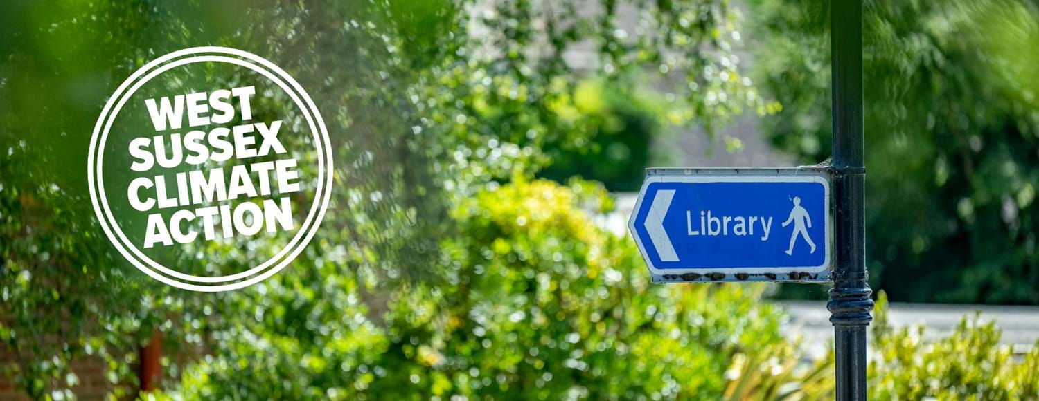 Library sign on pole with greenery and bushes and West Sussex Climate Action go in white