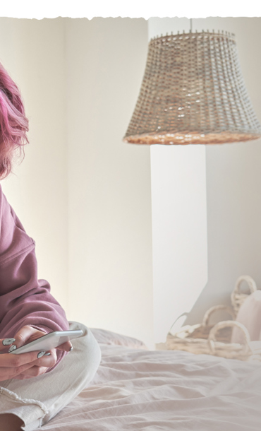 A young woman sat on a bed while looking at her mobile phone.