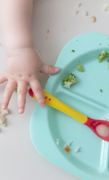 Child holding a spoon over a sectioned tray with food on it.