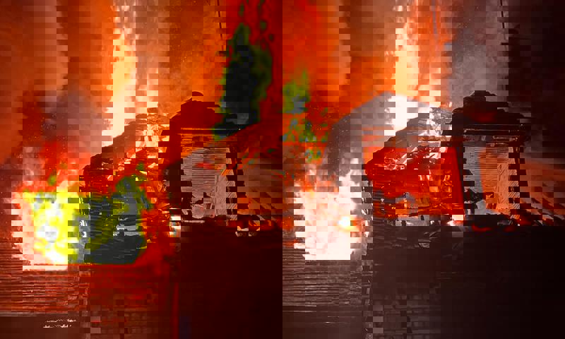 Photo of a house ablaze with flames above the roof.