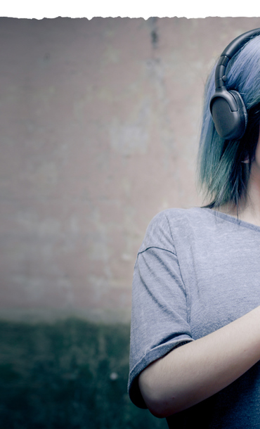 A young woman with headphones on wired to her mobile phone she's holding.