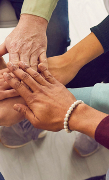 Seven people sat in a circle each with extended arms and hands overlapping.