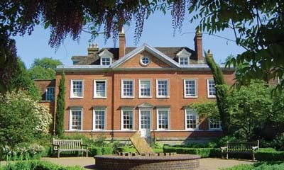 Large red brick house with white windows and frames and tree-lined garden to the front