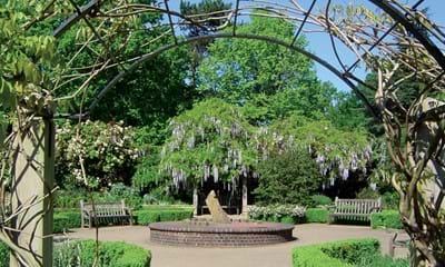 Scenic tree-lined circular garden area with archway, benches and central sculpture
