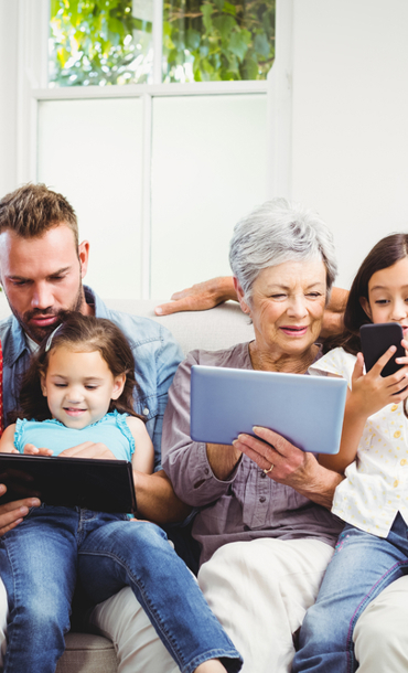 A family group of all ages sitting together using various digital devices