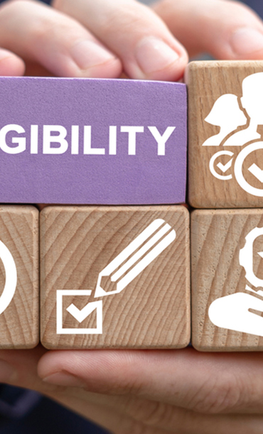 Person holding wooden blocks containing images and the word Eligibility