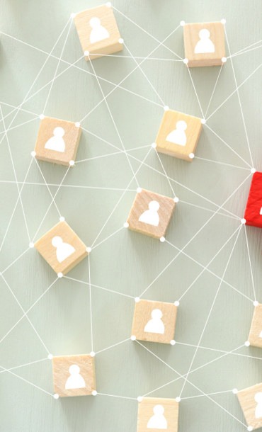 People icons on white cubes connected by lines One of the cubes is red and held by a hand.