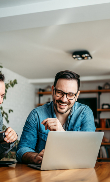 2 middle aged men looking at a computer screen and smiling.