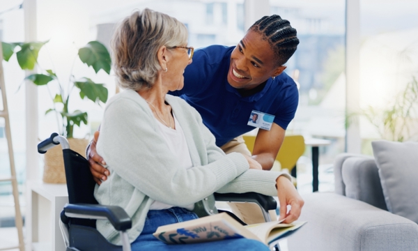 Young male caregiver in scrubs and elderly woman in wheelchair enthusiastically speaking together.