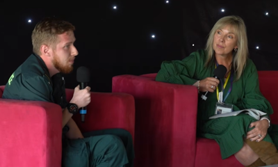 A male dressed in paramedic's uniform sits on a red armchair, talking to a lady dressed in green on the right.