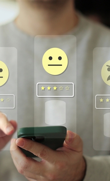 A person holding a smartphone with 5 icons of faces ranging from very unhappy with 5 stars underneath to very unhappy with 1 star underneath.