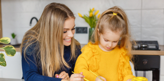 Young woman and small girl in yellow jumper painting pictures in a home setting.