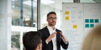 Man in suit presenting business strategy from a flipchart to team in office. 