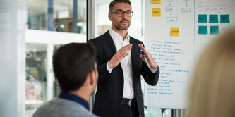 Man in suit presenting business strategy from a flipchart to team in office. 