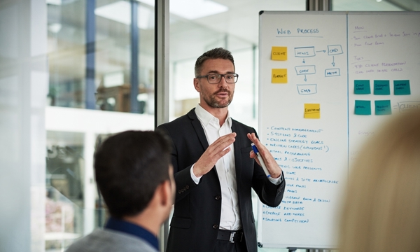 Man in suit presenting business strategy from a flipchart to team in office.