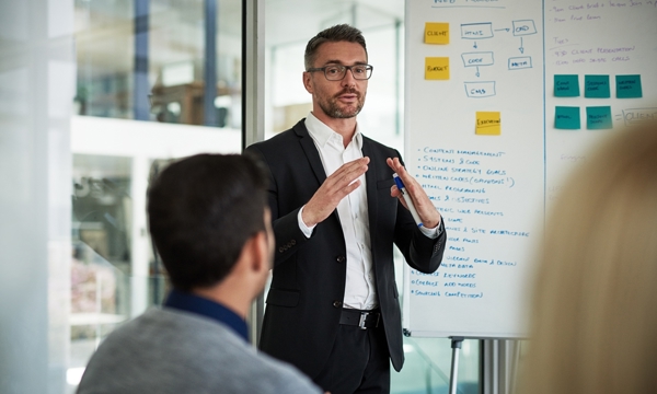 Man in suit presenting business strategy from a flipchart to team in office.