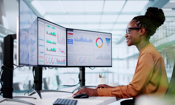 Female, young, black looking at three monitors, happy.