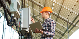 Young, male, caucasian working under solar panels checking electrics.
