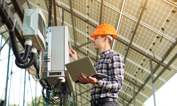 Young, male, caucasian working under solar panels checking electrics.