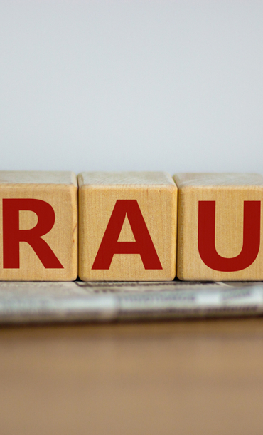 The word 'fraud' spelled with letters on blocks sitting on paperwork