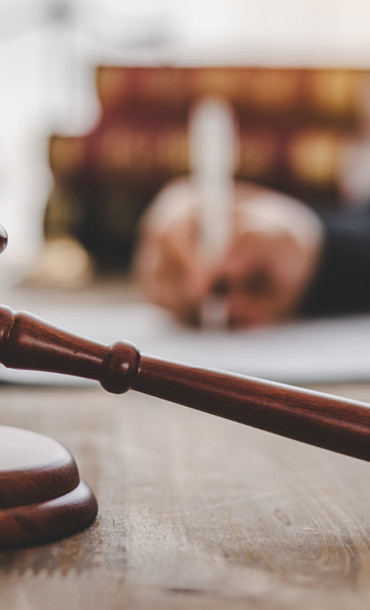 Judge sitting at a desk writing with books and a gavel in the foreground.
