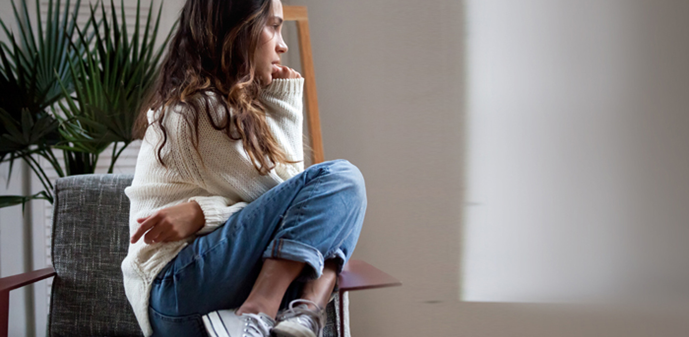 nojs A young woman with sat in a chair with her knees tucked up on the seat and her arms folded.
