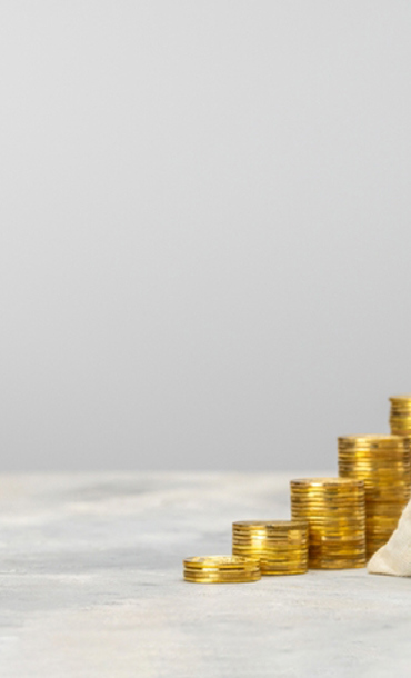 A tied bag of coins and a number of stacked gold coins, one with an education mortarboard hat on.