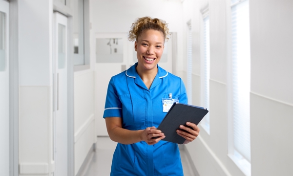 Female nurse in uniform standing in hospital corridor with clipboard smiling 